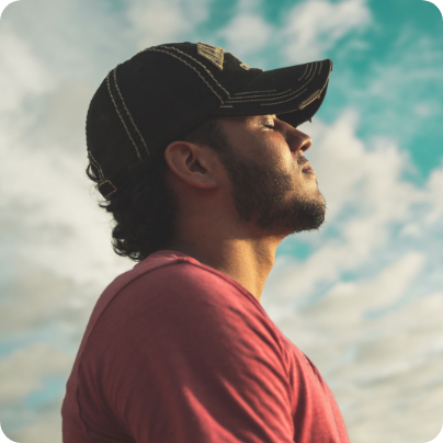 Ein Mann mit Kappe steht unter freien Himmel mit geschlossenen Augen.